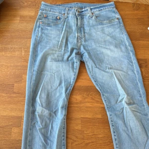 Levi's 502 ljusblå jeans W32 L32 - Ljusblå Levi's 502 jeans med klassisk femficksdesign och bruna sömmar. Jeansen har en rak passform och är tillverkade i mjukt denimtyg av bomull. Perfekta för dig som gillar en avslappnad men ändå stilren look.
