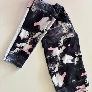 Mönstrade leggings från SOC - Säljer ett par leggings från SOC i storlek 146/152 med coolt abstrakt mönster i svart, vitt och rosa. De är tillverkade i ett stretchigt syntetmaterial som passar perfekt för träning eller chill. Snygg passform och bekväma att ha på sig hela dagen.