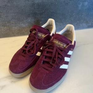 Adidas  Spezials - Säljer ett par vinröda Adidas Spezial sneakers i mocka med vita detaljer och klassiska tre ränder på sidorna. Skorna är i perfekt skick. Använda endast ett par gånger. Nypris 1399. 