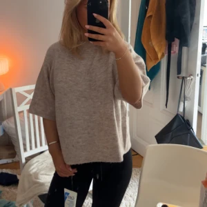 Beige stickad tröja med kort ärm - Säljer en beige stickad tröja med avslappnad passform och korta ärmar. Tröjan har en mjuk och skön känsla, perfekt för lager-på-lager och chill dagar. Enkel och stilren design som funkar till det mesta.