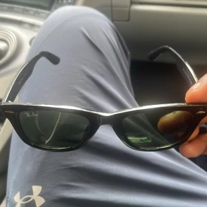 Svarta Ray-Ban Wayfarer solglasögon - Klassiska svarta Ray-Ban Wayfarer solglasögon med mörka glas. Snygg och tidlös modell med Ray-Ban-logga på båda sidorna. Tillverkade i Italien och har en robust plastbåge som ger en cool vibe till vilken outfit som helst.