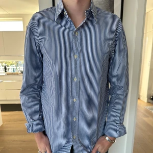 Randig skjorta från Polo Ralph Lauren - Snygg blåvit randig skjorta från Polo Ralph Lauren i slim fit. Skjortan är tillverkad i 100% bomull har klassisk krage, långa ärmar och knäppning framtill. Perfekt för en clean och stilren look. Grymt skick, inga defekter. Nypris 1799kr. Vårat pris 499kr. Storlek M. Modellen är 180cm. Skriv vid minsta intresse!