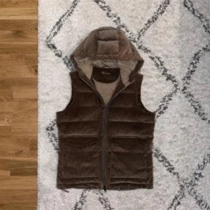 Stenströms väst Intressekoll - Snygg brun dunväst från Blauer i manchestertyg med horisontella quiltade paneler och praktisk huva. Västen har två stora fickor med lock framtill och stängs med dragkedja. Perfekt för lager-på-lager och chill stil.