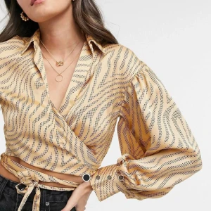 ASOS DESIGN omlottblus, stl 38 - Vacker blus från ASOS DESIGN i glänsande tyg med mjukt fall. Knyts i midjan.  Använd vid ett tillfälle, i mycket fint skick.  Storlek: 38 (UK 10)