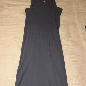 Mörkblå ribbad långklänning  - En stilren mörkgrå långklänning från 157 i ribbad 100% bomull. Ärmlös modell med rund halsringning och figurnära passform. Perfekt för dig som gillar enkel och clean stil med en twist av struktur i tyget. Klänningen är i storlek S