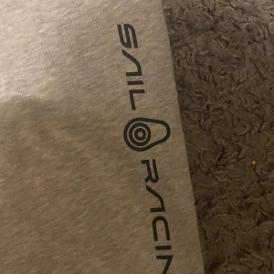 Grå mjukisbyxor från Sail Racing - Grå mjukisbyxor från Sail Racing med svart logga längs ena benet. Byxorna har snörning i midjan och är tillverkade i mjukt bomullsmaterial. Perfekta för chill eller träning, med klassisk passform och ribbade muddar vid bensluten.