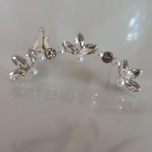 Silvriga ear cuff med pärlor och kristaller - Snygga ear cuffs i silverfärg med glittrande kristaller och små vita pärlor. Blommig design med tre kristallblad och pärldetaljer som klättrar längs örat. Perfekt accessoar för dig som vill sticka ut med något extra. Endast 1!<3