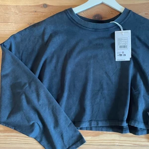 Croppad långärmad tröja Stronger  - Svart/grå croppad långärmad tröja från Stronger med diskret logga framtill. I nyskick, endast testad! 