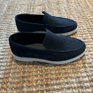 Marinblå loafers i mocka - Snygga marinblå loafers i mocka från Zara. De har en stilren design med en vit sula som ger en modern touch. Perfekta för en avslappnad men ändå stilfull look. Endast använda en gång.