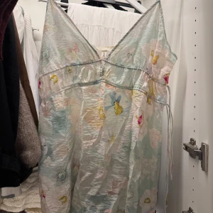 Pastellblommig långklänning H&M - Superfin långklänning från H&M i pastelliga toner med blommigt mönster. Klänningen har v-ringning, tunna axelband och en luftig, flowy passform. Perfekt för varma dagar och somriga vibes. Materialet är lätt och känns svalt mot huden.