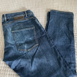 Oscar Jacobson Jeans - Snygga blå jeans från Oscar Jacobson i klassisk denim med raka ben och normal passform. Jeansen har fem fickor, bälteshällor och en stilren läderpatch bak i midjan. Perfekt för dig som gillar tidlös och clean stil.