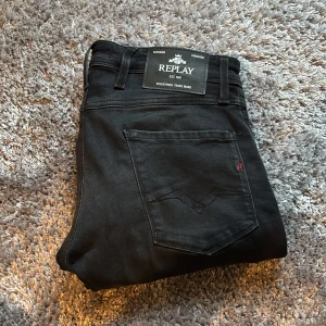 Svarta Replay Anbass  - Svarta Replay Anbass jeans med slim fit och klassisk femficksdesign. Snygga detaljer som Replay-logga på fickan och bakre läderpatch. Jeansen har raka ben och är tillverkade i mjukt stretchigt bomullsmaterial för skön passform. Tveka inte att höra av dig vid frågor eller fler bilder!
