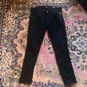 Svarta Replay Anbass jeans, storlek 32/32 - Säljer ett par svarta Replay Anbass jeans i storlek 32. De har en slim passform med klassisk femficksdesign och snygga detaljer vid fickorna. Jeansen är tillverkade i mjukt jeansmaterial och har en rak siluett som sitter snyggt på benen. Midja 41cm längd 101cm (27)