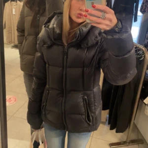 Svart pufferjacka med dragkedja - Säljer en svart pufferjacka från superdry med luva, fickor och dragkedja. Jackan är snyggt kroppsformad och perfekt för kallare dagar. Jag hittar inte lappen med storleken men jag skulle säga att den passar XS-M