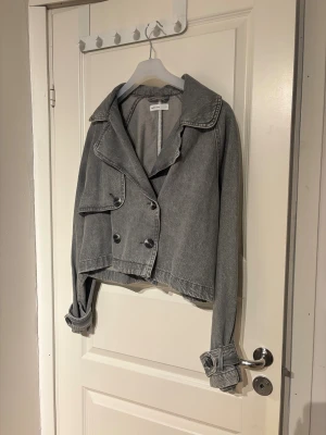 Grå croppad jeansjacka från Ginatricot  - Säljer en grå croppad jeansjacka från Ginatricot med dubbelknäppning framtill och bred krage. Jackan har långa ärmar med knappar vid mudden och en avslappnad, loose passform. Perfekt för dig som gillar en edgy och trendig look!!💖         Den är inte så jätte lång, men oversized  Storlek: S  Som ny🩶
