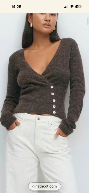 Brun omlottkofta från Gina Tricot - Mysig brun omlottkofta från Gina Tricot med djup v-ringning och dekorativa knappar på sidan. Tröjan är stickad, har lång ärm och en croppad passform som ger en trendig look. 🥰