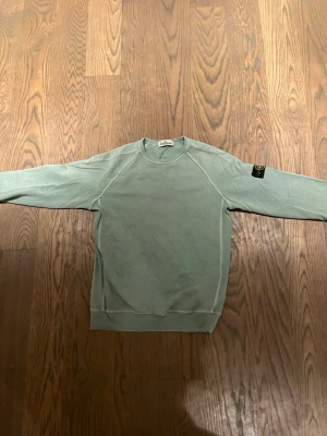 Grön sweatshirt från Stone Island Junior - Säljer en äkta Snygg grön sweatshirt från Stone Island Junior med klassisk rund hals och ribbade muddar. Tröjan har den ikoniska Stone Island-patchen på vänster ärm och är tillverkad i mjuk bomull. Perfekt för dig som gillar streetwear och vill ha en clean look.