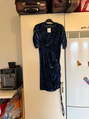 Mörkblå sammetsklänning H&M - Supersnygg mörkblå sammetsklänning från H&M med kort ärm och snörningsdetalj på sidan. Klänningen har en figurnära passform och är i kort modell. Perfekt för dig som vill sticka ut med en lyxig känsla och cool textur. Helt ny med tags/ prislapp fortfarande kvar. 