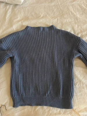 Blå ribbad stickad tröja NA-KD - Säljer en blå stickad tröja från NA-KD i storlek XS. Tröjan har ett ribbat mönster, långärmade ärmar och en något högre hals