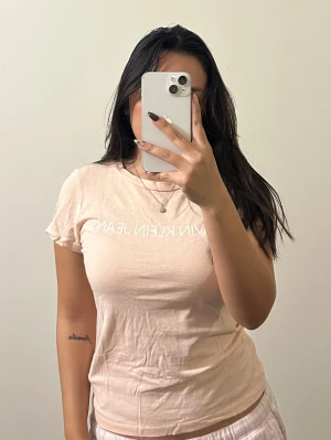 Ljusrosa Calvin Klein Jeans t-shirt - Snygg ljusrosa t-shirt från Calvin Klein Jeans med vit logotyp framtill. Modellen är klassisk med rund hals och korta ärmar. Mjuk och skön bomull som sitter normal på kroppen. Strl XS men passar även mig som är S. Skriv vid frågor 🥰