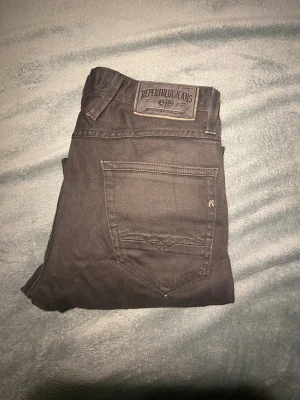 Svarta Replay Anbass jeans, W30 L30 - Svarta Replay Anbass jeans i klassisk femficksmodell med dragkedja fram. Slimmad passform och snygga detaljer på bakfickan. Tillverkade i mjukt jeanstyg som sitter skönt hela dagen. Perfekta för dig som gillar stilrena och moderna jeans.