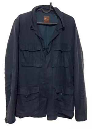 Mörkblå Stenströms overshirt i linne - Snygg marinblå overshirt från Stenströms i storlek M (passar mer som L), tillverkad i linne. Jackan har fyra stora fickor framtill, klassisk krage och knäppning med mörka knappar. Fodret är i blankt blått tyg och en broderad detalj syns i nacken. Notera att mittersta knappen gått sönder men funkar! Pris ej hugget i sten!