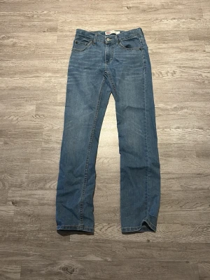 Levi's 511 blå jeans straight fit - Säljer ett par klassiska Levi's 511 jeans i ljusblå tvätt. Modellen har rak passform, fem fickor och knappgylf. Jeansen är tillverkade i mjukt bomullsdenim och har den ikoniska Levi's-lappen bak i midjan. Perfekt för en chill och stilren look.