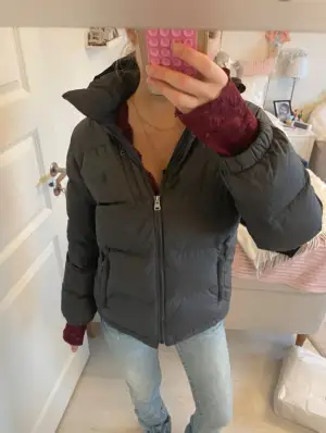 Säljer en mörkgrå dunjacka från Polo Ralph Lauren med huva och dragkedja framtill. Jackan har broderad logga på bröstet, två sidofickor med dragkedja och en bröstficka. Puffad design och elastiska muddar vid ärmslut. Perfekt för kalla dagar!