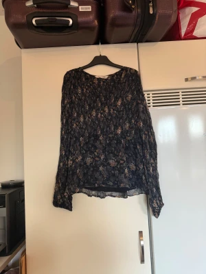 Blommig svart blus med långa ärmar - Säljer en flowy svart blus med blommigt mönster i beige, grönt och lila. Blusen har långa, transparenta ärmar med resår vid ärmslut och en lätt rynkad struktur. Perfekt för dig som gillar boho-vibe och mjuka material. Från märket Odd Molly. Storlek 2 som enligt deras storleksguide motsvarar en M. Mycket fint skick, jag hittar inga synliga anmärkningar eller defekter.  