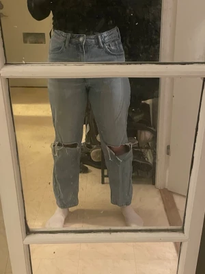 Ljusblå ripped jeans med raka ben - Säljer ett par ljusblå jeans med raka ben och höga knän med slitna hål. Klassisk femficksmodell och hög midja. Jeansen har en relaxed passform och är tillverkade i jeansmaterial. Perfekt för dig som gillar en chill och trendig look. 158 cm lång i benen 