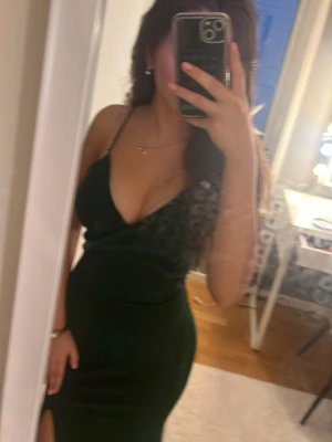 Mörkgrön långklänning med snörning - Supersnygg mörkgrön glittrig  långklänning från hellomolly med smala axelband, v-ringning och slits framtill. Klänningen har öppen rygg med korsad snörning som ger en riktigt elegant vibe. 