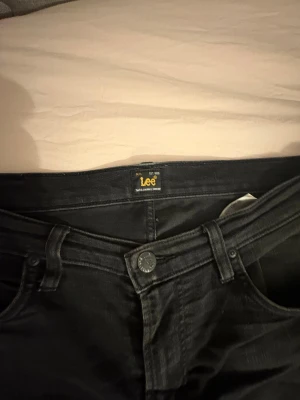 Svarta Lee Rider jeans W32 L32 - Säljer ett par svarta Lee Rider jeans i klassisk femficksmodell. Jeansen har raka ben, normal passform och är tillverkade i mjukt denimtyg. Perfekta för dig som gillar en stilren look med diskreta detaljer och snygg svart tvätt.