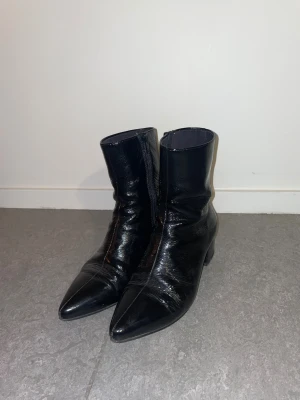 Svarta stövletter från Vagabond - Säljer ett par svarta stövletter från Vagabond med glansig finish och spetsig tå. Skorna har låg klack, dragkedja på sidan och är tillverkade i skinn. Snygg och stilren modell som passar perfekt till höstens outfits.