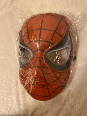 Spiderman mask  - Cool Spiderman mask i röd med svarta linjer och stora svarta ögonpartier. Masken har ett klassiskt spindelnätsmönster och är perfekt för cosplay eller maskerad. Tillverkad i syntetmaterial och har en snygg form som täcker hela ansiktet. Finns fler kvar 