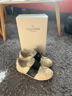 Valentino Garavani Open sneakers, vit/marinblå - Säljer ett par Valentino Garavani Open sneakers i vitt skinn med bred marinblå läderdetalj över snörningen. Klassisk rund tå och platt sula. Kommer med originalkartong och dustbag. Perfekta för dig som vill ha en clean men lyxig look.