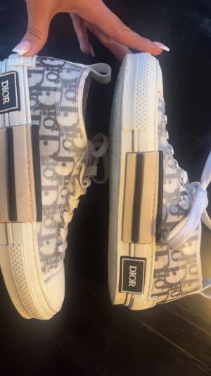 Dior sneakers. Byter gärna mot storlek 35 eller 36 - byter gärna mot samma skor eller sånna skor men i svart vitt i 35 eller 36.                                                       Säljer ett par Dior sneakers i grå och vit. Skorna har en rund tå och svart detalj på sidan av sulan. Pris kan diskuteras