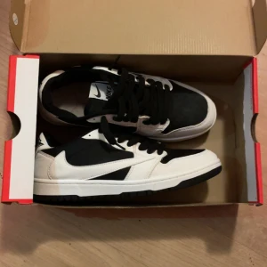 Nike dunk Travis Scots - Nike Dunk Low sneakers i svart och vitt med klassisk design. Skorna har svart tåparti och snörning, vita paneler och svart sula. Tillverkade i skinn och syntetmaterial, med låg profil och rund tå. Perfekta för dig som gillar streetwear och stilrena färgkombinationer.höstskor