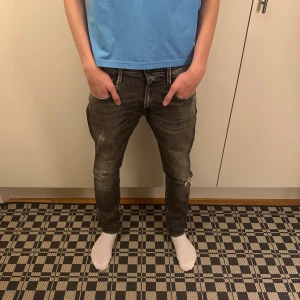 Svarta Replay jeans med slitningar - Säljer ett par svarta Replay jeans med snygga slitningar och tvättade detaljer. Jeansen har klassisk femficksdesign, raka ben och normal passform. Materialet är jeans och de har tydliga sömmar på bakfickorna. Perfekta för en cool och avslappnad stil.