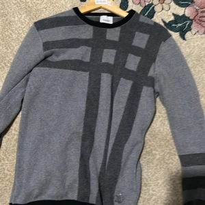 Grå tröja från Burberry - Säljer en snygg grå tröja från Burberry med ett coolt rutmönster i mörkare grå nyanser. Tröjan har långa ärmar och en rund halsringning. Perfekt för både vardag och lite finare tillfällen. Passar bra till jeans eller chinos!