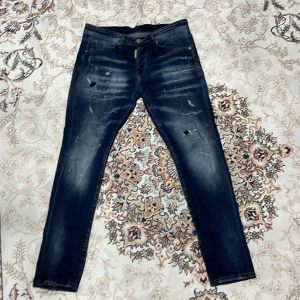 Dsquared2 Mörkblå Jeans  - Säljer ett par mörkblå skinny jeans med coola slitningar och lätt tvättade detaljer. Jeansen har klassisk femficksdesign och smal passform som sitter tajt längs benen. Perfekta för dig som gillar en trendig och avslappnad look.