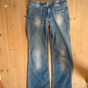 Lågmidjade bootcut jeans ljusblå - Ljusblå jeans med låg midja och bootcut-ben. Snygga slitningar framtill och bakfickor med dekorativa sömmar. Klassisk femficksmodell med breda hällor och dragkedja. Perfekta för en avslappnad och trendig    Jeansen är från början köpta från Vinted, men säljs pga de ej passade. 