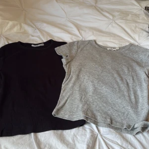 2-pack ribbade toppar grå & svart - Säljer två basic ribbade toppar i storlek 146/152. En är ljusgrå och en är svart, båda med rund halsringning och korta ärmar. Perfekta att matcha med jeans eller kjol för en enkel och clean look.