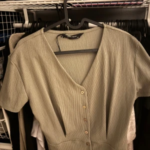 Beige ribbad kortklänning LCW Vision - Kortklänning i beige från LCW Vision, storlek XS. Klänningen har ribbad struktur, v-ringning och knappar framtill. Kortärmad och figurnära passform som ger en clean och stilren look. Perfekt för dig som gillar minimalistisk stil.