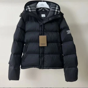 Svart dunjacka från Burberry - Säljer en svart dunjacka från Burberry med klassiskt rutigt foder i huvan. Jackan har dragkedja, knappar och två fickor framtill. Puffig modell med lång ärm och logga på ärmen. Perfekt för kalla dagar och riktigt snygg streetstil.