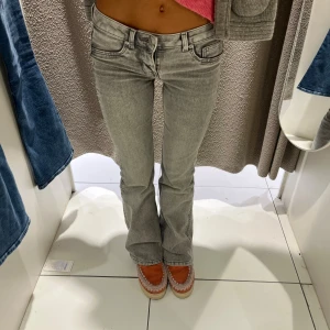 Grå bootcut jeans med låg midja - Snygga grå jeans med bootcut och låg midja. Jeansen har klassisk femficksdesign och är tillverkade i ett mjukt denimtyg. Perfekta för dig som gillar en retro vibe och vill ha ett par jeans som sticker ut lite extra.