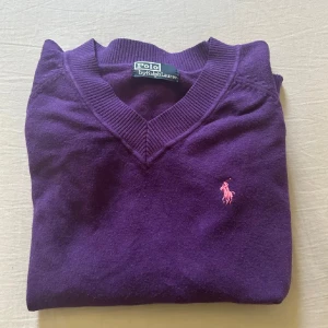  Polo Ralph Lauren 100% Cashmere - Säljer en lila v-ringad tröja från Polo Ralph Lauren 100% Cashmere med rosa broderad logga på bröstet. Tröjan är långärmad och har ribbade muddar vid ärmslut och nederkant. Tillverkad i mjuk ull, perfekt för kyliga dagar. Obs endast swish betalning nuläget skickas spårbart 59kr