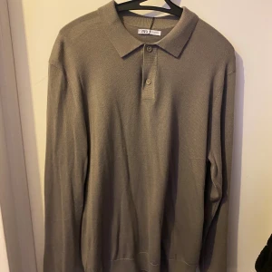 Beige pikétröja från Zara i M - Stilren beige pikétröja från Zara i storlek M. Tröjan har klassisk krage, knäppning med två knappar och långa ärmar. Tillverkad i mjukt material som känns skönt mot huden. Perfekt för en clean och avslappnad look.