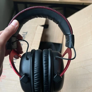 HyperX Cloud II Gaming Headset - HyperX Cloud II gaming headset med avtagbar mikrofon, bekväma öronkuddar och robust aluminiumram. Klassisk svart och röd design. Headsetet ser ut att vara i gott skick utan synliga skador eller slitage. Perfekt för gaming och kommunikation.
