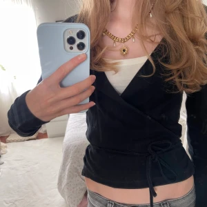 Svart omlottopp från Envii - Säljer jättesnygg Svart omlottopp från Envii med långa ärmar och knyt i midjan. Toppen har en v-ringad design och är tillverkad i ribbad bomull. 