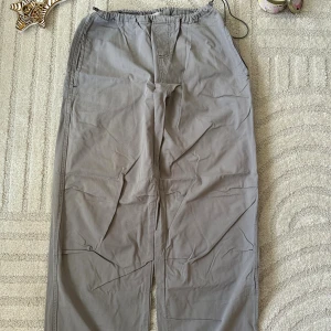 Grå cargopants med dragsko - Säljer ett par grå cargopants med elastisk midja och dragsko i benslut. Byxorna har raka ben och är tillverkade i ett mjukt bomullstyg. Perfekta för en chill och avslappnad stil.